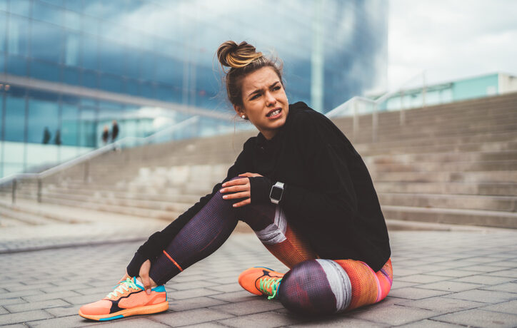 Woman with pain in the leg during workout sitting on ground.