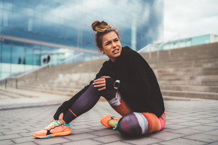 Woman with pain in the leg during workout sitting on ground.