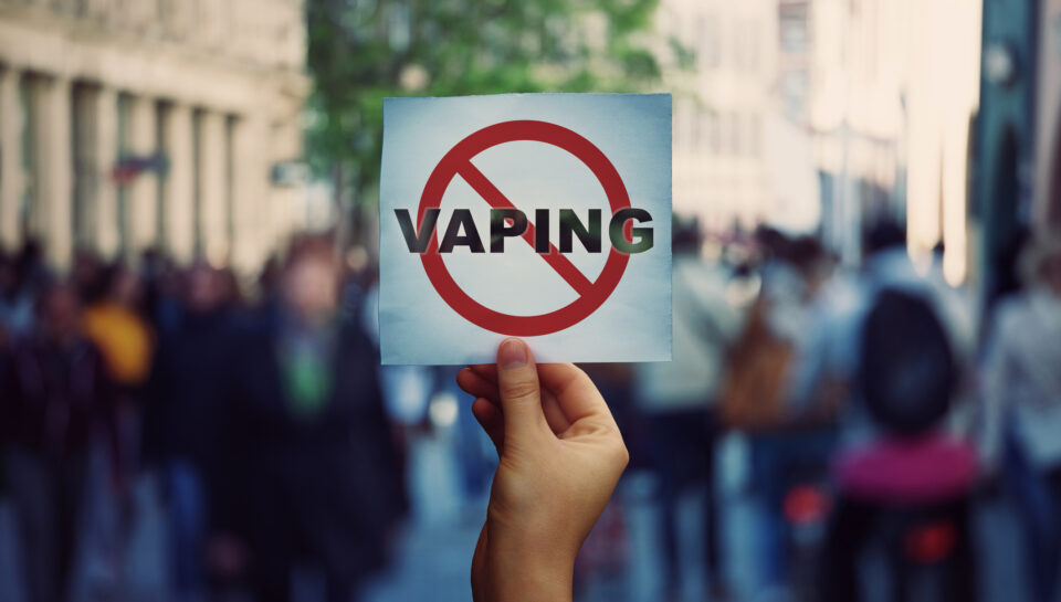 Human hand holding a protest banner stop vaping message over a crowded street background. Banning flavored vaping products to discourage people from smoking electronic cigarettes. Health risk concept.